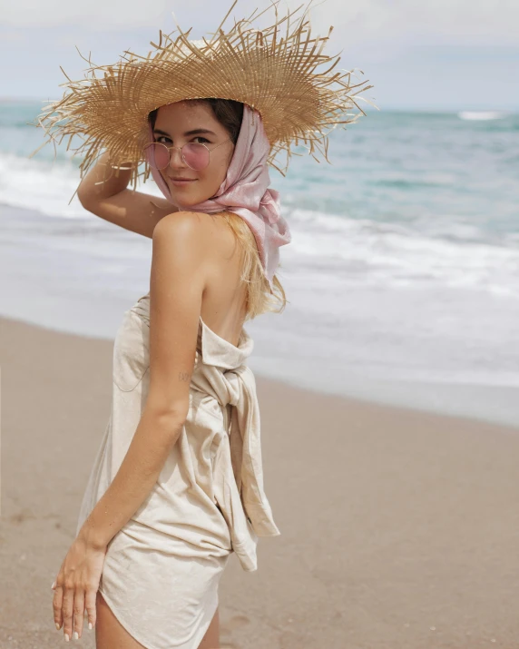 a woman standing on top of a sandy beach, natural skin tones, wearing a turban, modeled, linen