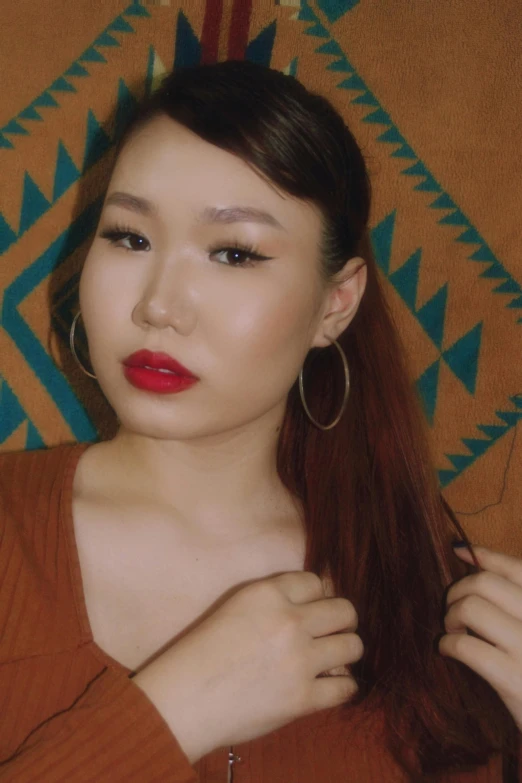 a woman in a brown shirt is straightening her hair, an album cover, inspired by Yang J, instagram, thick red lips, profile image, jewelry, half asian