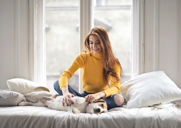 a woman sitting on a bed petting a dog, pexels contest winner, yellow clothes, wearing turtleneck, redhead woman, wearing a white sweater