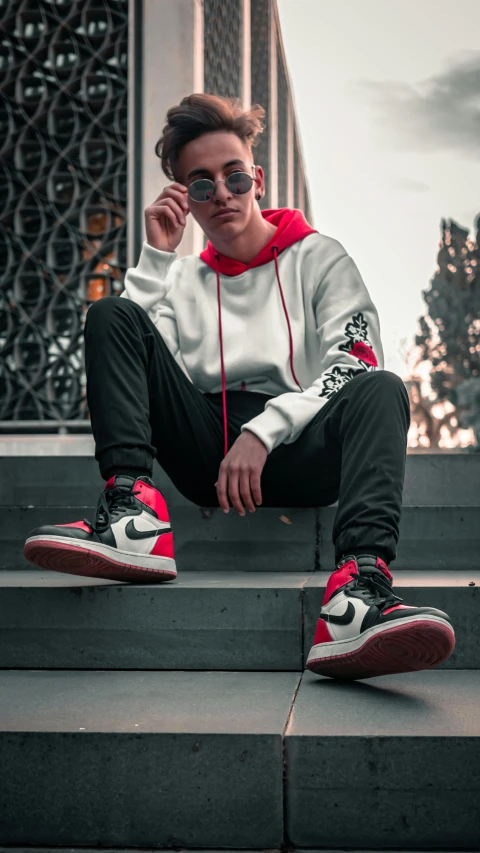 a person sitting on some steps talking on a cell phone, inspired by Jordan Grimmer, trending on pexels, black red white clothes, “air jordan 1, avatar image, confident pose