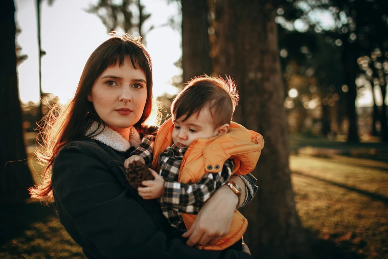 a woman holding a baby in her arms, a portrait, by Emma Andijewska, pexels, at a park, avatar image, serious expression, warm coloured