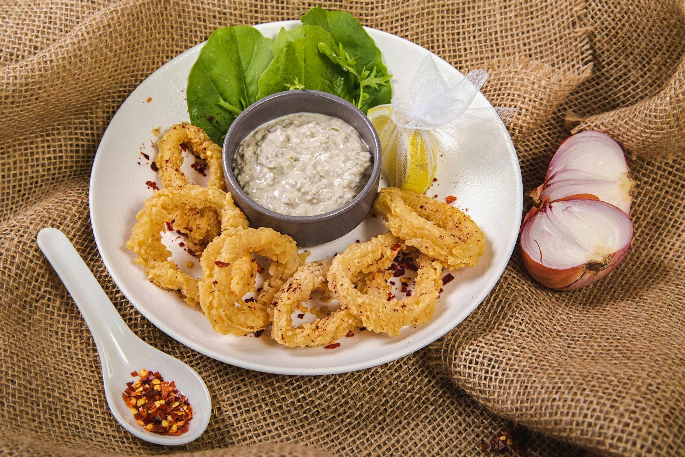 a white plate topped with onion rings next to a bowl of dip, hurufiyya, fish hooks, thumbnail, malaysian, linen