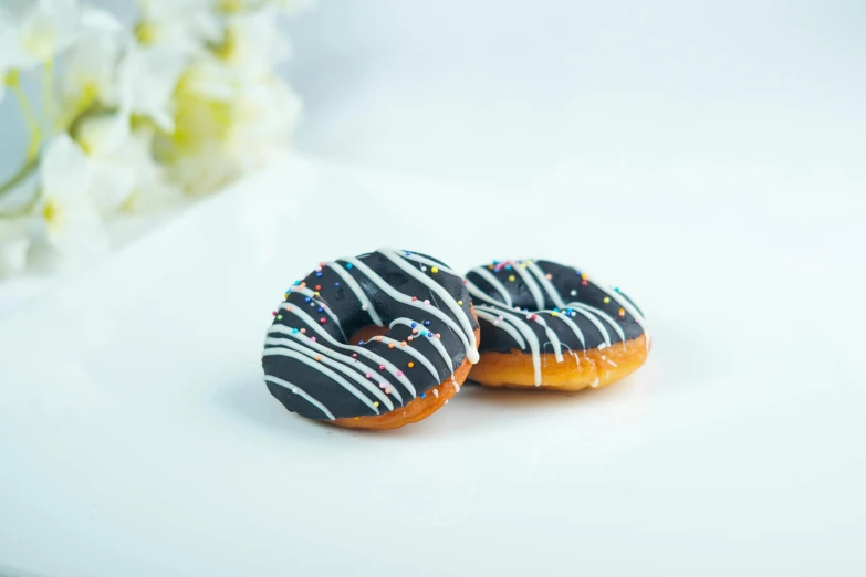 a couple of donuts sitting on top of a white table, product image, black and orange, vista view, chocolate