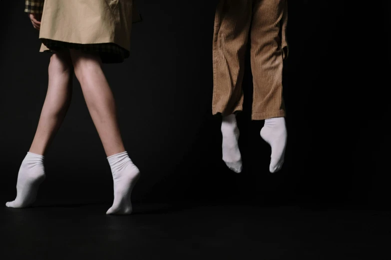 a couple of women standing next to each other, an album cover, by Maciej Kuciara, unsplash, socks, standing with a black background, khakis, runway photo