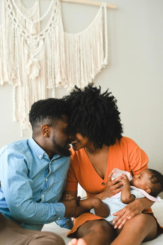 a man and woman sitting on a bed with a baby, by Carey Morris, pexels contest winner, renaissance, black man with afro hair, kissing each other, pictures of family on wall, caring fatherly wide forehead