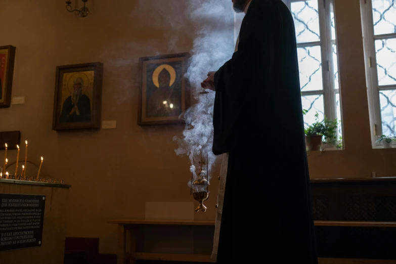 a priest holding a lit candle in a church, by Attila Meszlenyi, pexels contest winner, smoking a magical bong, 👰 🏇 ❌ 🍃, black robe, at home