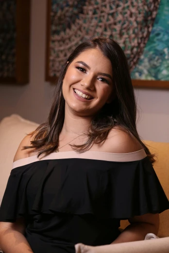 a woman in a black dress sitting on a couch, fernanda suarez, smiling young woman, profile image, 1 9 year old