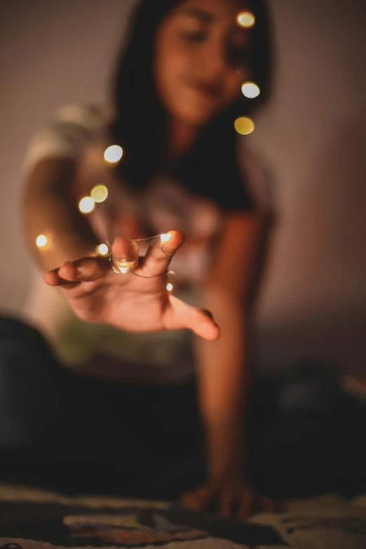 a woman sitting on top of a bed holding a lit candle, pexels contest winner, light and space, fairy lights, hands reaching for her, blurred, 2019 trending photo