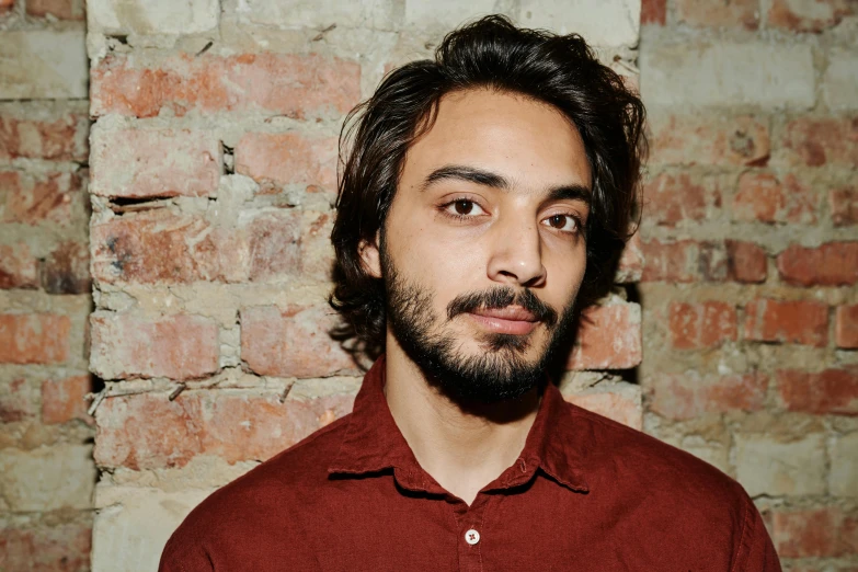 a man standing in front of a brick wall, an album cover, pexels contest winner, antipodeans, light stubble with red shirt, mahmud barzanji, headshot profile picture, 15081959 21121991 01012000 4k