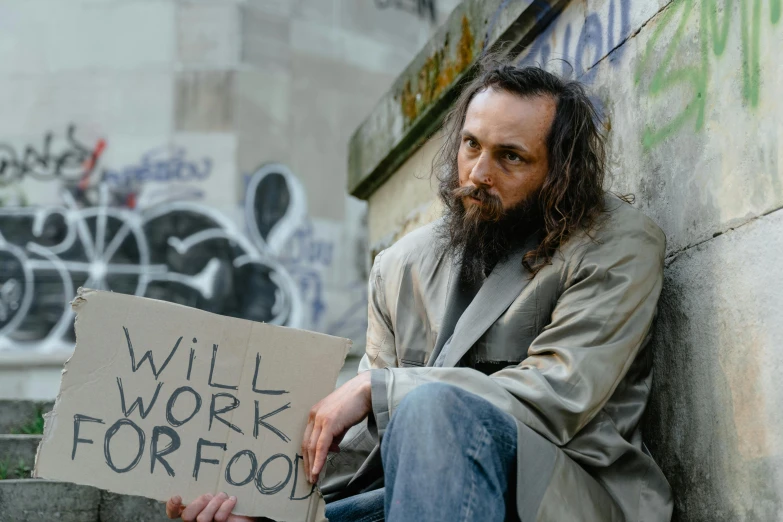 a man holding a sign that says will work for food, an album cover, unsplash, stuckism, cyberpunk homeless, getty images, joaquin phoenix, barefoot