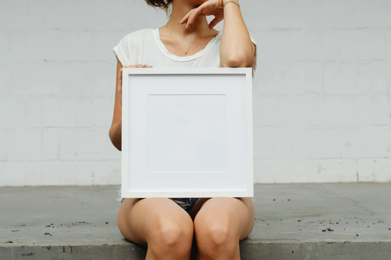 a woman sitting on a step holding a picture frame, inspired by Ellsworth Kelly, unsplash contest winner, full lenght view. white plastic, square, single flat colour, white finish