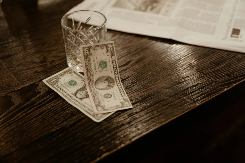 a glass filled with money sitting on top of a wooden table, sitting on a table, dollar bill, thumbnail, no watermarks