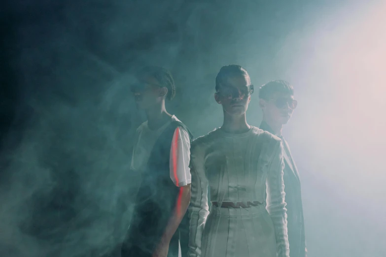 a group of people standing next to each other on a stage, an album cover, by Emma Andijewska, pexels contest winner, bauhaus, futuristic glasses lenses, smoke filled room, still from a music video, fashion studio lighting