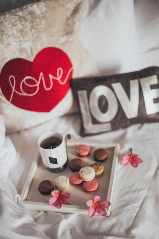 a tray of cookies and a cup of coffee on a bed, a colorized photo, by Julia Pishtar, trending on pexels, romanticism, love is begin of all, cushions, saying, u