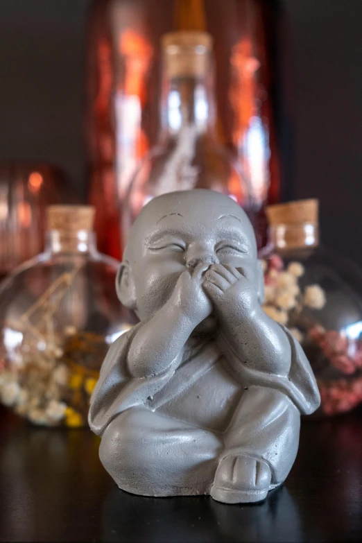 a small figurine sitting on top of a table, a statue, inspired by Anne Geddes, unsplash, hand over mouth, clay amulets, grey, product display photograph