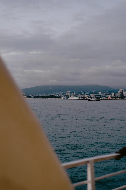 a man standing on top of a boat next to a body of water, the sea seen behind the city, stormy snowy fiji mountain, shot on anamorphic lenses, shaped like a yacht