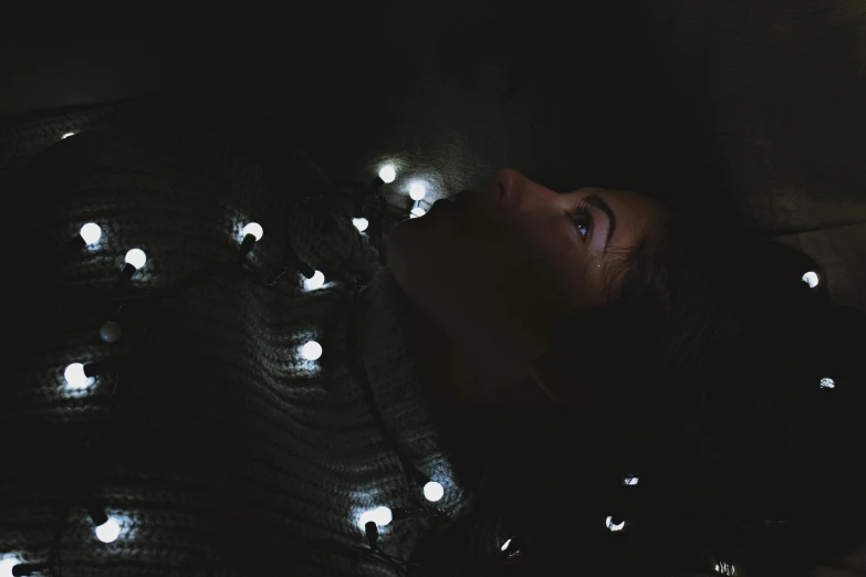 a woman laying on top of a bed covered in lights, a black and white photo, trending on pexels, light and space, hanging out with orbs, tactile buttons and lights, scary mood, intricate led jewellery