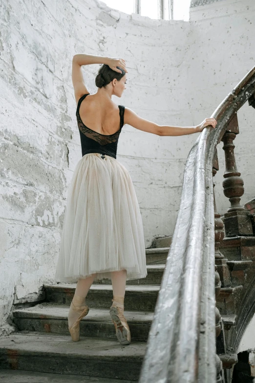 a woman that is standing on some stairs, arabesque, wearing a tutu, curated collections, back arched, grey