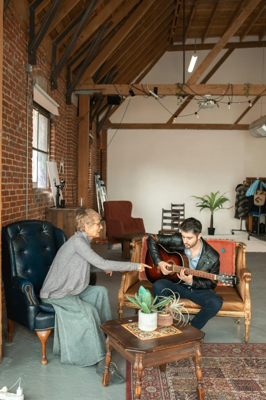 a man playing a guitar next to a woman sitting in a chair, by Everett Warner, pexels contest winner, interior of a loft, comforting, artsationhq, plain background