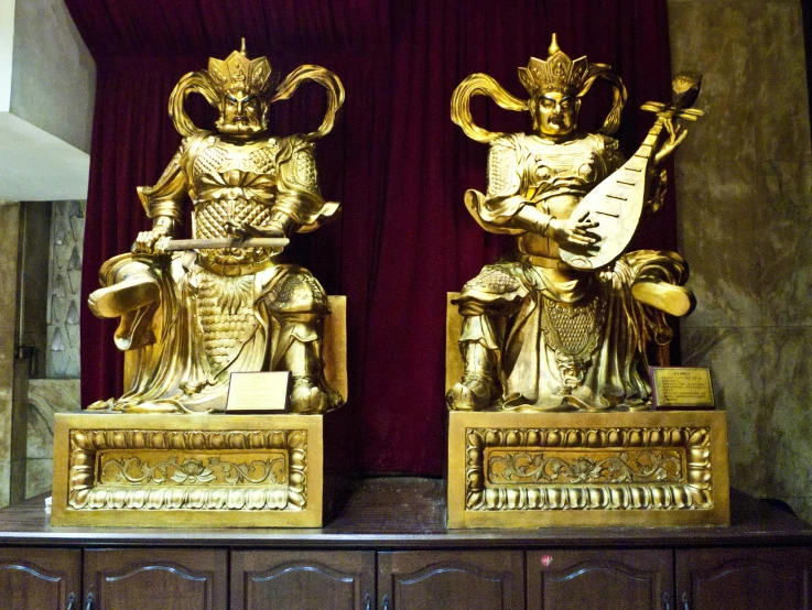 a couple of gold statues sitting on top of a wooden table, a statue, in style of pan ren wei, diabolus in musica, organs, very symmetrical