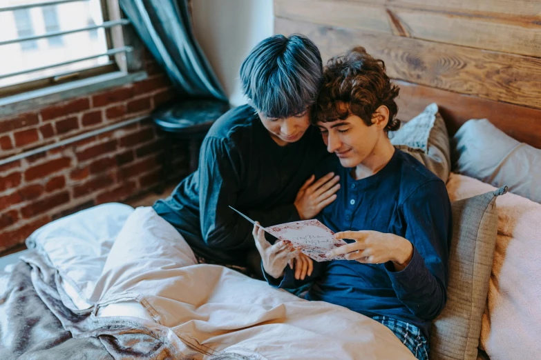a couple of young men sitting on top of a bed, by Julia Pishtar, trending on pexels, renaissance, reading the book about love, andy milonakis, avatar image, holding each other