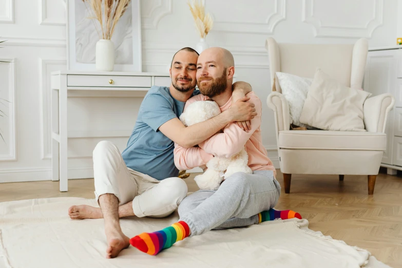 a man sitting on the floor holding a baby, by Julia Pishtar, pexels contest winner, two men hugging, pride month, avatar image, couple on bed