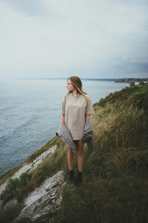 a woman standing on top of a cliff next to the ocean, muted colors. ue 5, casual clothing, canvas, poncho