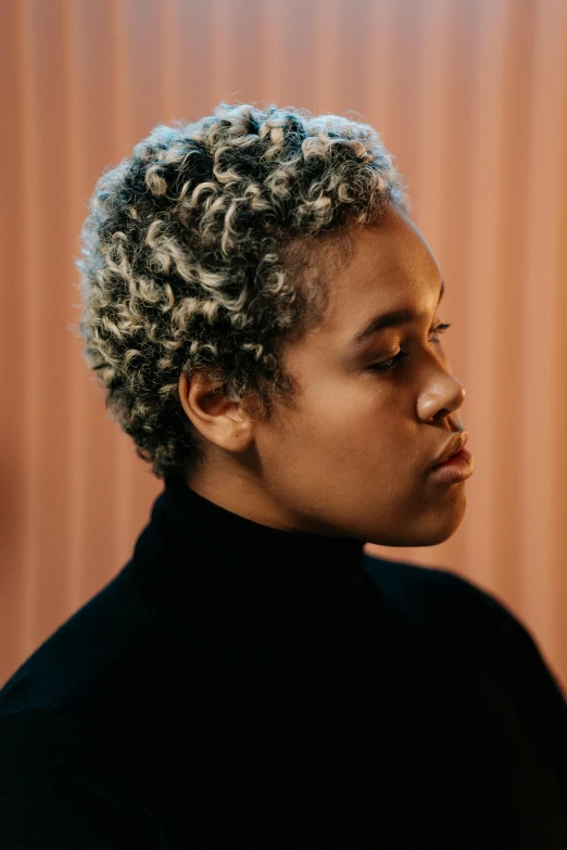 a woman with curly hair standing in front of a wooden wall, trending on pexels, realism, short platinum hair tomboy, wearing a turtleneck and jacket, mixed-race woman, concert