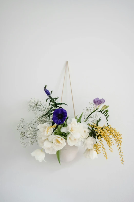 a white vase filled with purple and white flowers, by Jessie Algie, minimalism, hanging from white web, white with gold accents, white and yellow scheme, with a soft