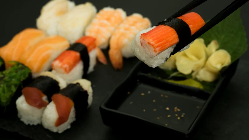 a black plate topped with sushi and chopsticks, multicoloured, 5 fingers, black and orange, unbeatable quality