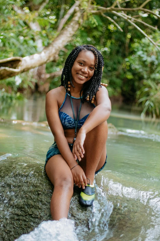 a woman sitting on a rock in a river, by Lily Delissa Joseph, relaxing and smiling at camera, jamaican vibe, bralette, profile image