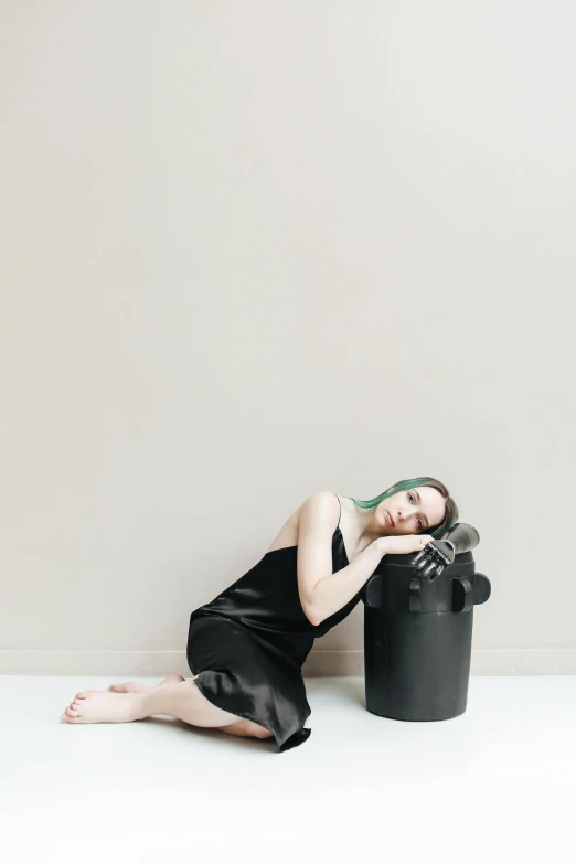 a woman laying on the floor next to a trash can, by Nina Hamnett, unsplash, conceptual art, in front of white back drop, tuba, dark black porcelain skin, sitting on top of a cryopod