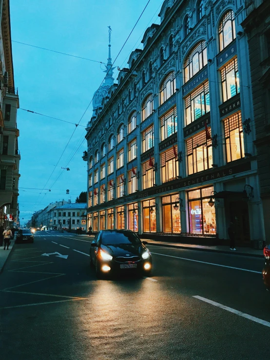 a car driving down a street next to tall buildings, by Julia Pishtar, pexels contest winner, helsinki, des boutiques avec des neons, high detailed store, 000 — википедия