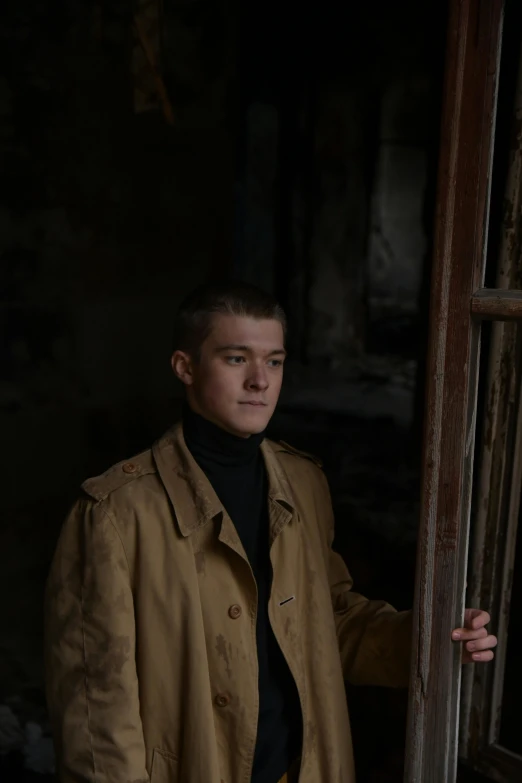 a man in a trench coat standing by a window, a character portrait, by Attila Meszlenyi, promo still, male teenager, standing in abandoned building, brown buzzcut