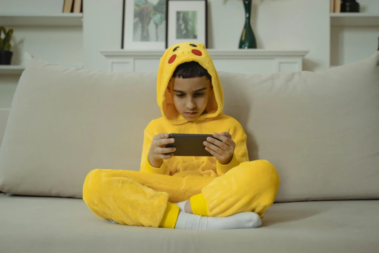 a child in a pikachu costume sitting on a couch, a cartoon, inspired by Abidin Dino, pexels, looking at his phone, namco, gif, uk