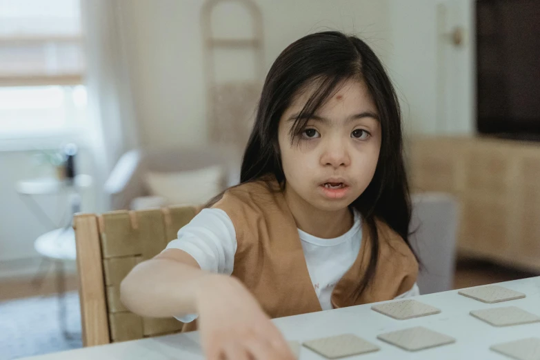 a little girl that is sitting at a table, trending on pexels, mingei, ability image, tabletop game board, neutral expressions, tactile