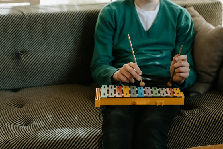 a man sitting on a couch playing a musical instrument, trending on pexels, kinetic art, childrens toy, xylophone, overcast mood, school class