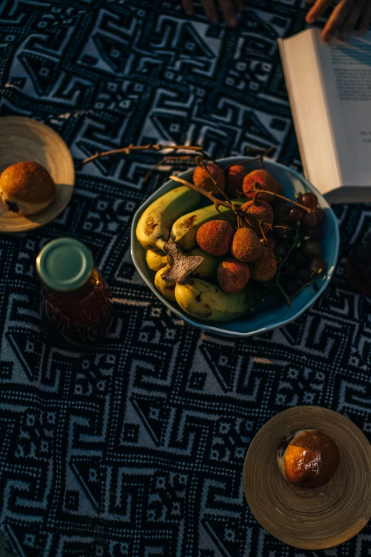 a table topped with a bowl of fruit next to a book, african arts, food, at twilight, high camera angle