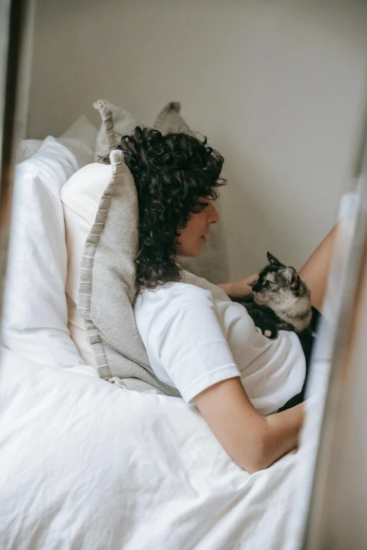 a woman laying in bed with a cat, pexels contest winner, curls, light beige pillows, profile image, in a comfortable chair