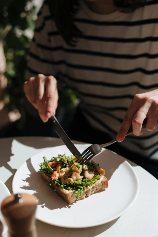 a woman sitting at a table with a plate of food, pexels contest winner, eating garlic bread, greens), sleek hands, cutlery