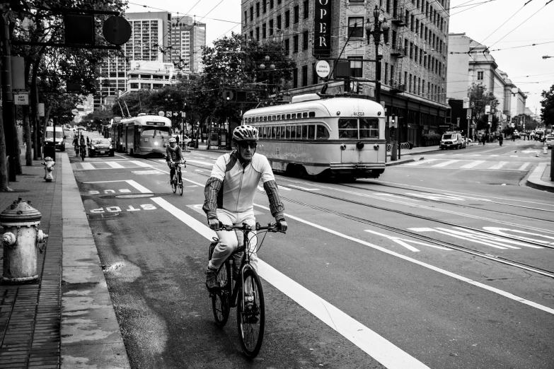 a man riding a bike down a street next to a bus, a black and white photo, cascadia, square, sports photo, tourist photo