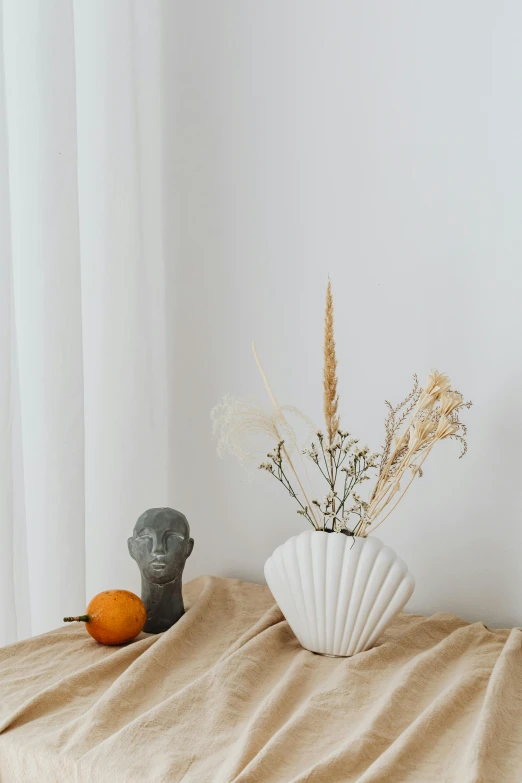 a white vase sitting on top of a wooden table, a marble sculpture, trending on pexels, wearing seashell attire, made of dried flowers, in a white boho style studio, indoor picture