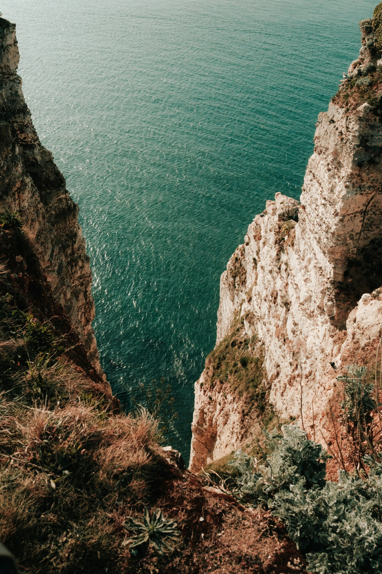 a person standing on top of a cliff next to the ocean, steep cliffs, top down camera angle, teal aesthetic, ravine