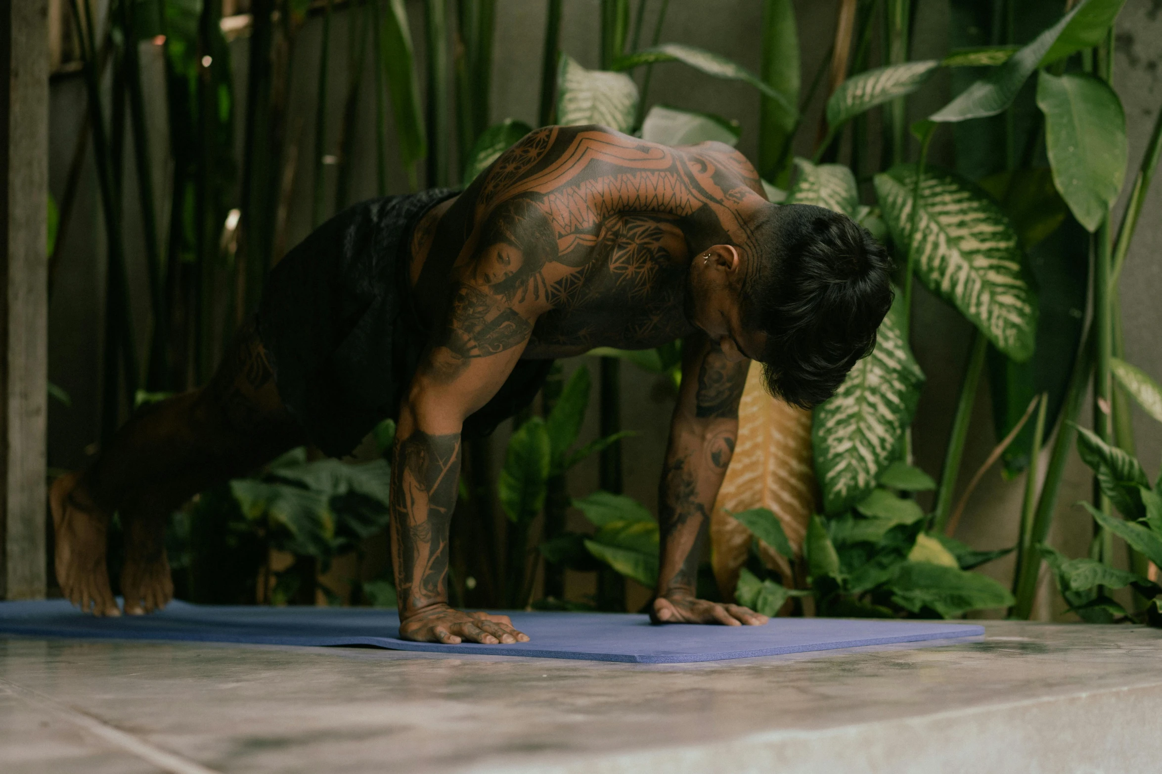 a man doing a yoga pose on a blue mat, a tattoo, covered in plants, from 8 k matte, brown body, asian male