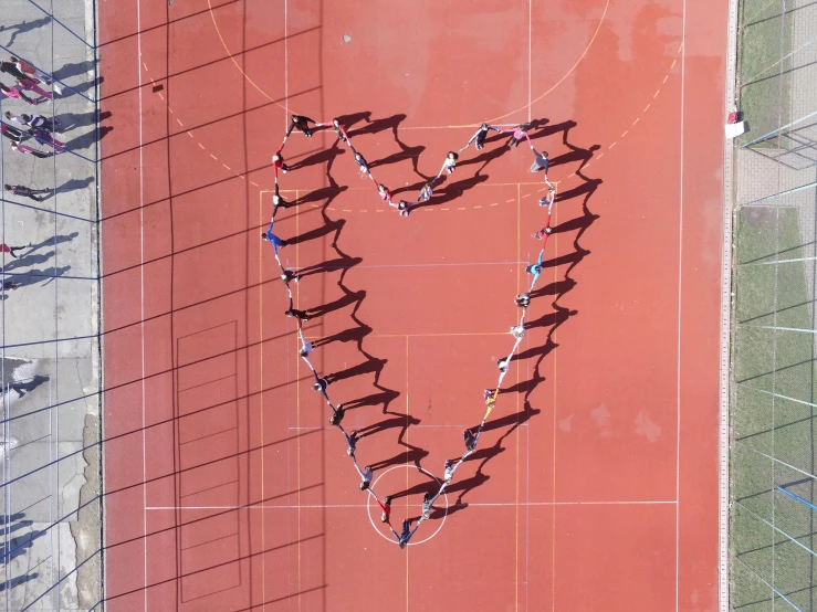 a group of people standing on top of a tennis court, by Attila Meszlenyi, pexels contest winner, land art, forming a heart with their necks, school class, “diamonds, public art