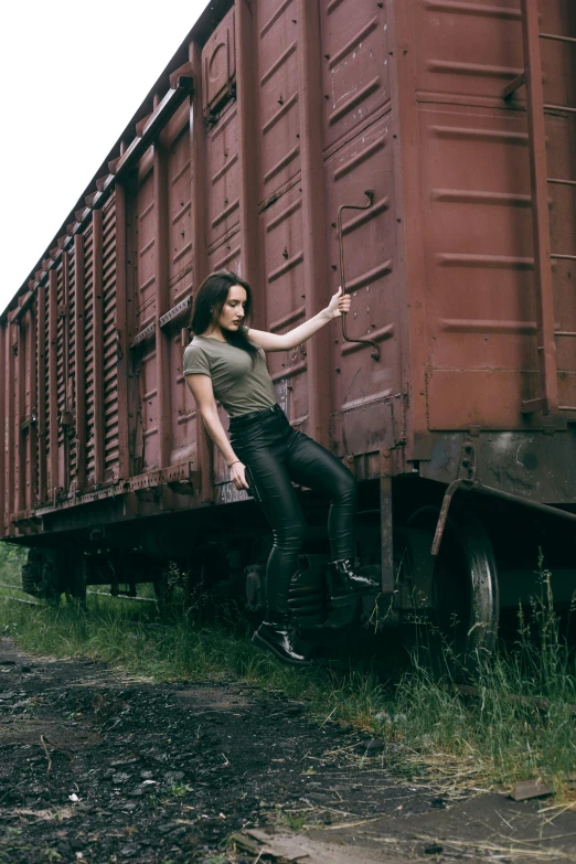 a woman leaning against the side of a train, an album cover, by Adam Marczyński, pexels contest winner, fighter pose, silo, full body pose, rugged