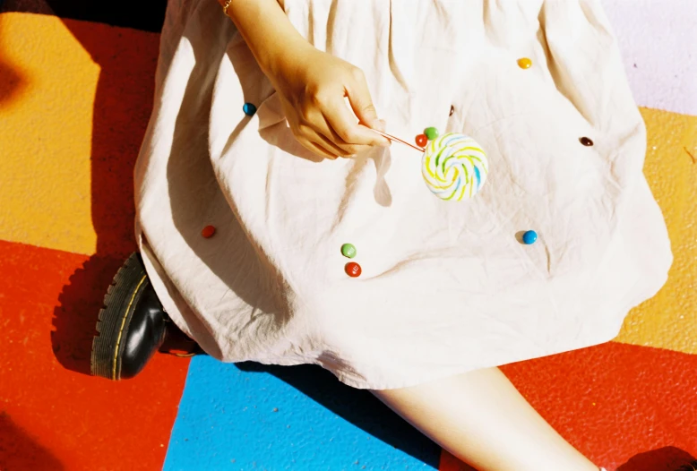 a little girl sitting on the floor with a lollipop lollipop lollipop lollipop lollipop lollipop lo, an album cover, by Nathalie Rattner, trending on pexels, magic realism, wide skirts, james jean and petra cortright, color 3 5 mm, on a canva