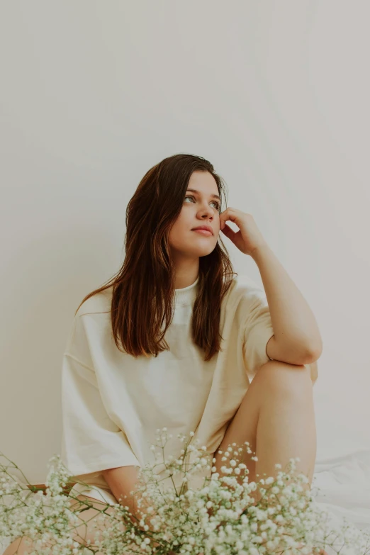 a woman sitting on a bed with a bouquet of flowers, an album cover, trending on unsplash, minimalism, with brown hair, looking to the side off camera, wearing a white sweater, thinker pose