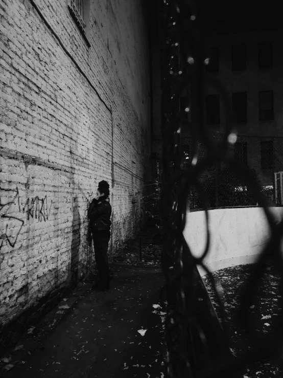 a person standing in front of a brick wall, a black and white photo, by Adam Rex, unsplash contest winner, graffiti, late night melancholic photo, dormant in chains, night. by greg rutkowski, shot on expired instamatic film