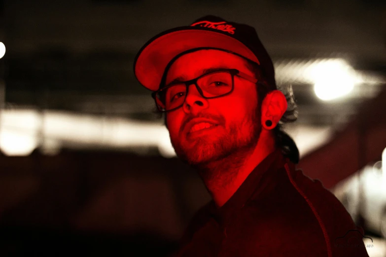 a man wearing a red hat and glasses, by Matt Cavotta, red led lights, profile pic, asher duran, backroom background